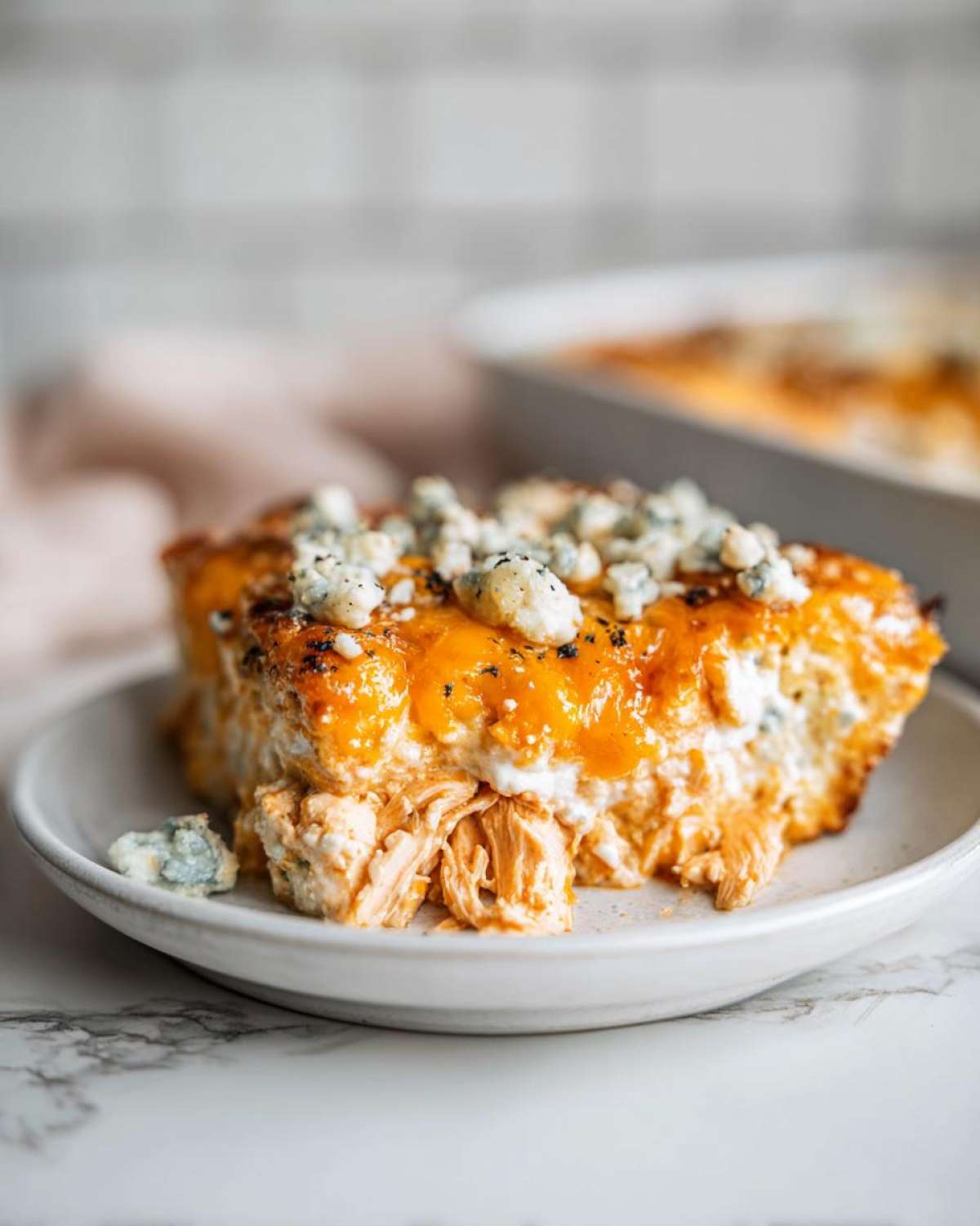 A close-up serving of Keto Creamy Buffalo Chicken Casserole topped with melted cheddar and blue cheese crumbles.
