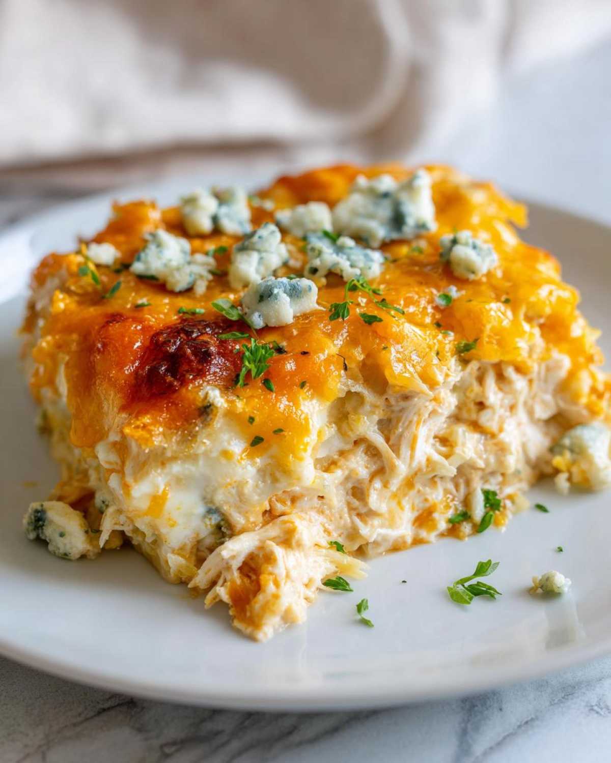 A close-up serving of Keto Creamy Buffalo Chicken Casserole topped with melted cheddar and blue cheese crumbles.