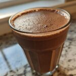 Close-up of a glass filled with a thick, frothy Keto Creamy Chocolate Peanut Butter Shake.