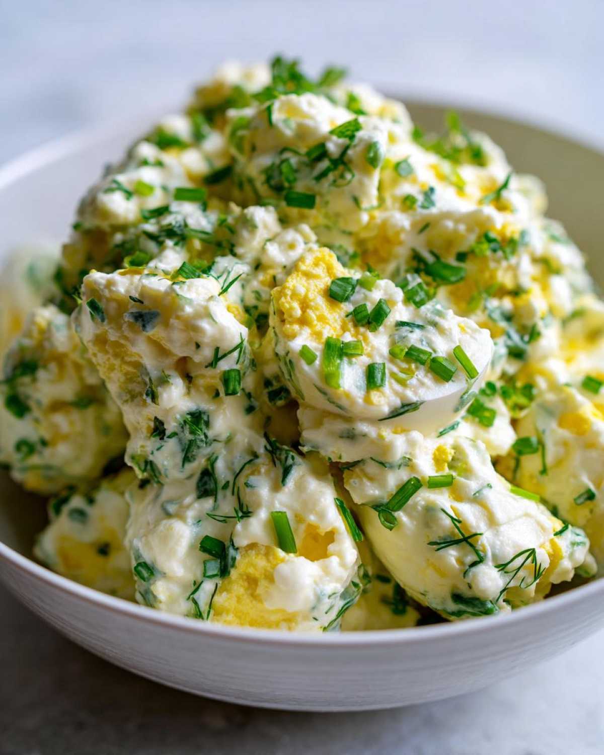 Close-up of chunky Keto Creamy Herb Deviled Egg Salad mixed with creamy dressing and topped with fresh chopped chives.