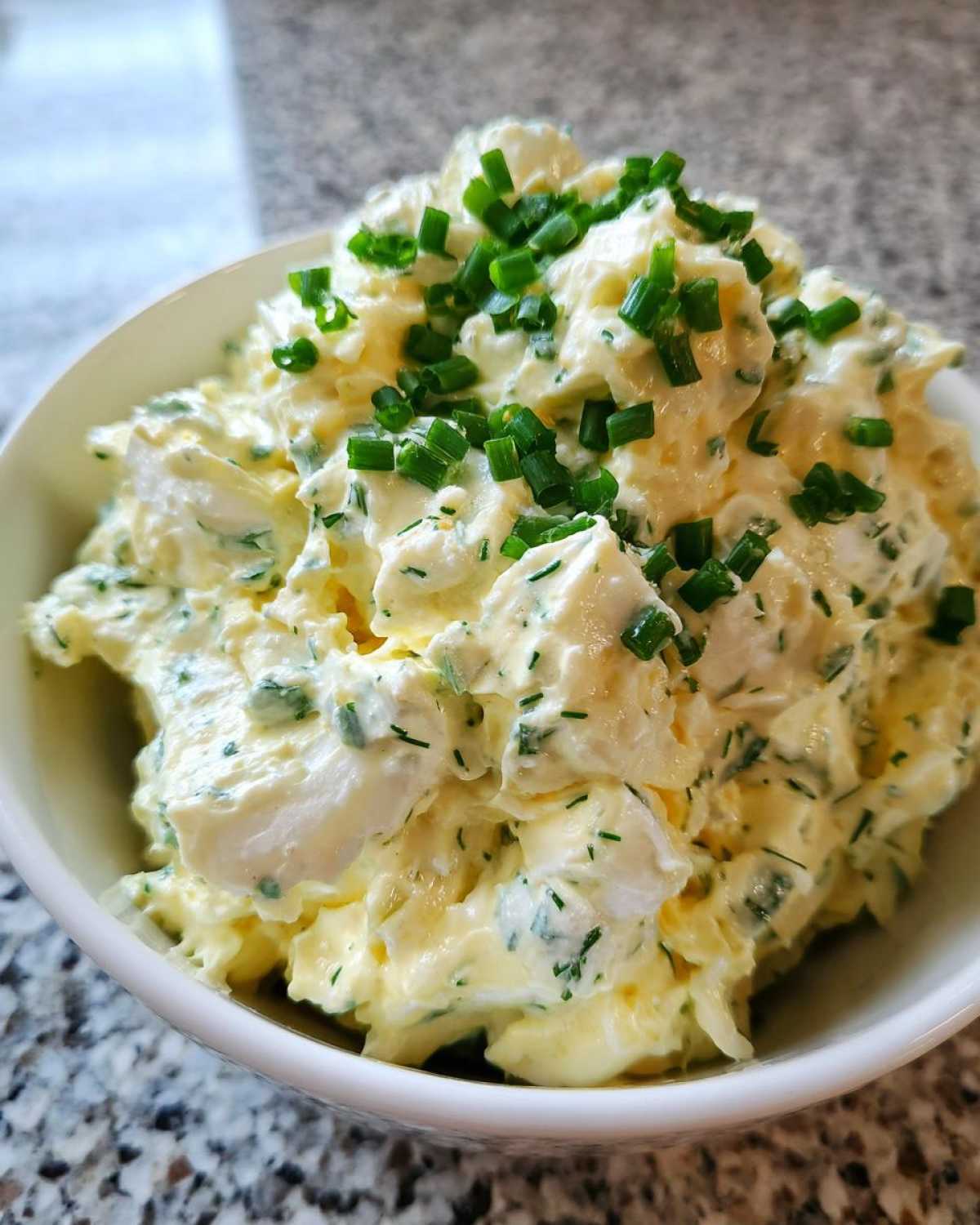 A close-up view of rich Keto Creamy Herb Deviled Egg Salad topped generously with fresh chopped chives.
