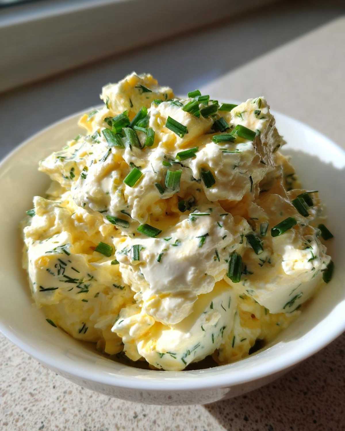 Close-up of Keto Creamy Herb Deviled Egg Salad, topped generously with fresh chopped chives, served in a white bowl.