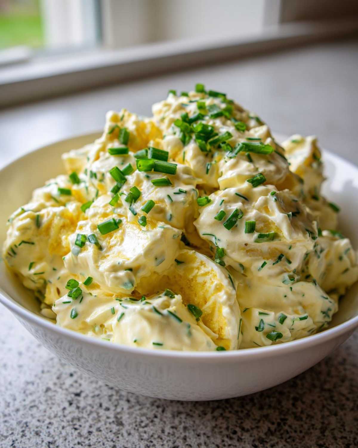 Close-up of Keto Creamy Herb Deviled Egg Salad generously topped with fresh chopped chives in a white bowl.