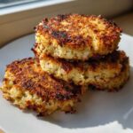 A stack of three golden-brown, crispy Keto Crispy Cauliflower Hash Browns on a white plate.