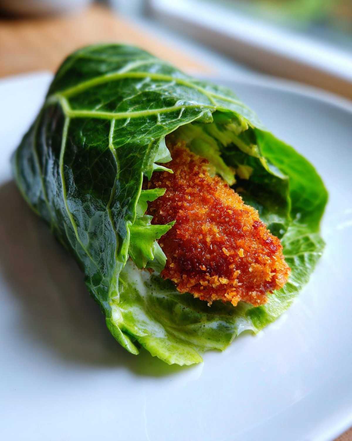 A single Keto Crispy Chicken Caesar Salad Wrap made with a large green leaf wrapper holding crispy chicken and Caesar dressing.