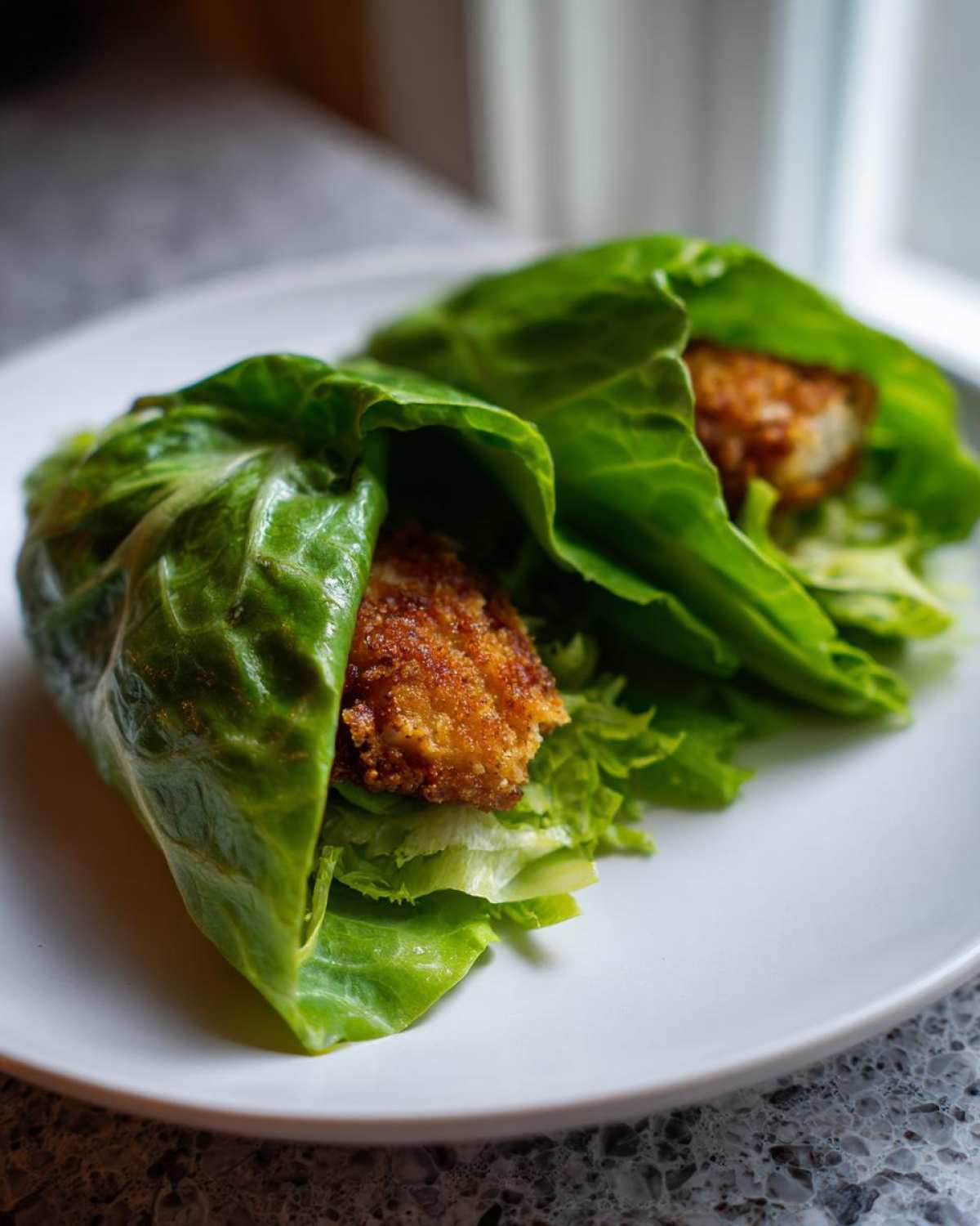 Two Keto Crispy Chicken Caesar Salad Wraps made with large lettuce leaves and golden fried chicken pieces.