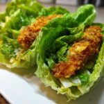 Two Keto Crispy Chicken Caesar Salad Wraps made with romaine lettuce cups filled with crispy chicken tenders and dressing.
