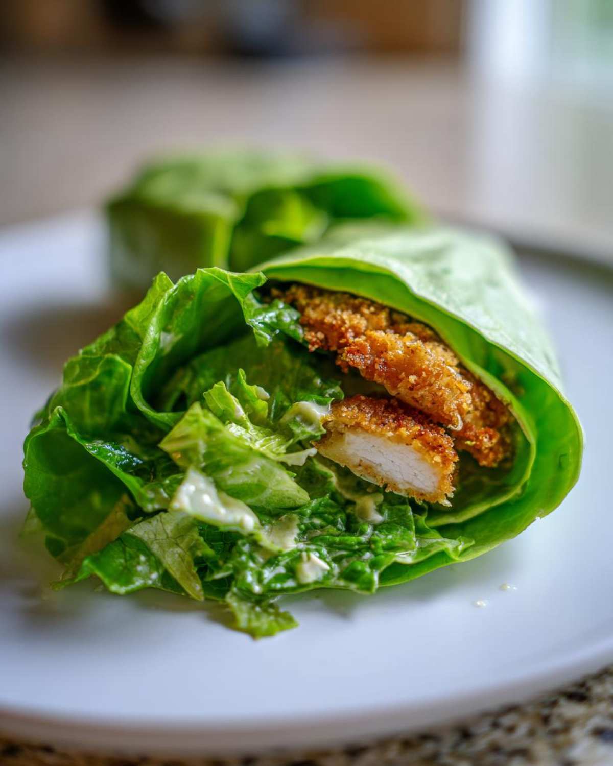 A close-up of a Keto Crispy Chicken Caesar Salad Wrap made with crisp lettuce leaves, creamy dressing, and breaded chicken strips.