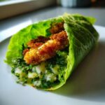 Close-up of one Keto Crispy Chicken Caesar Salad Wraps, featuring crispy chicken strips nestled in a romaine lettuce leaf with creamy dressing and greens.