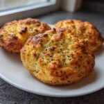 Three golden-brown Keto Everything Bagel Cloud Breads topped with black poppy seeds resting on a white plate.