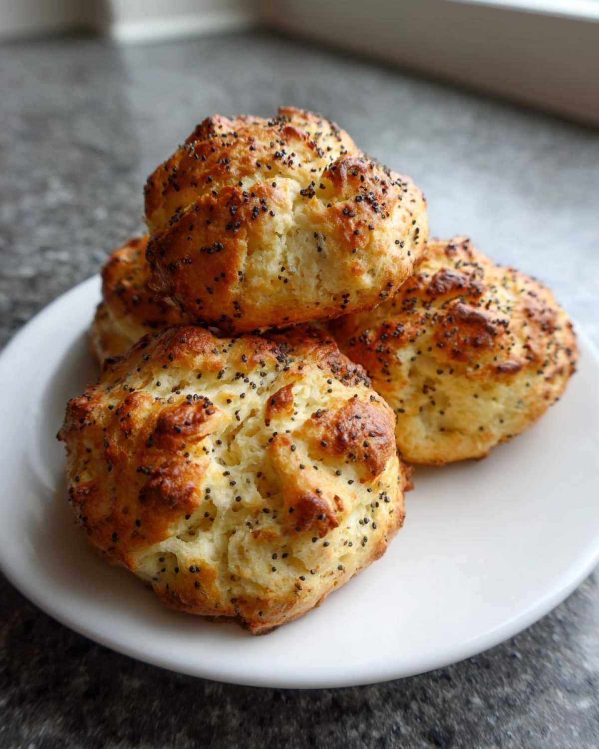 A stack of golden brown Keto Everything Bagel Cloud Bread pieces topped with poppy seeds resting on a white plate.
