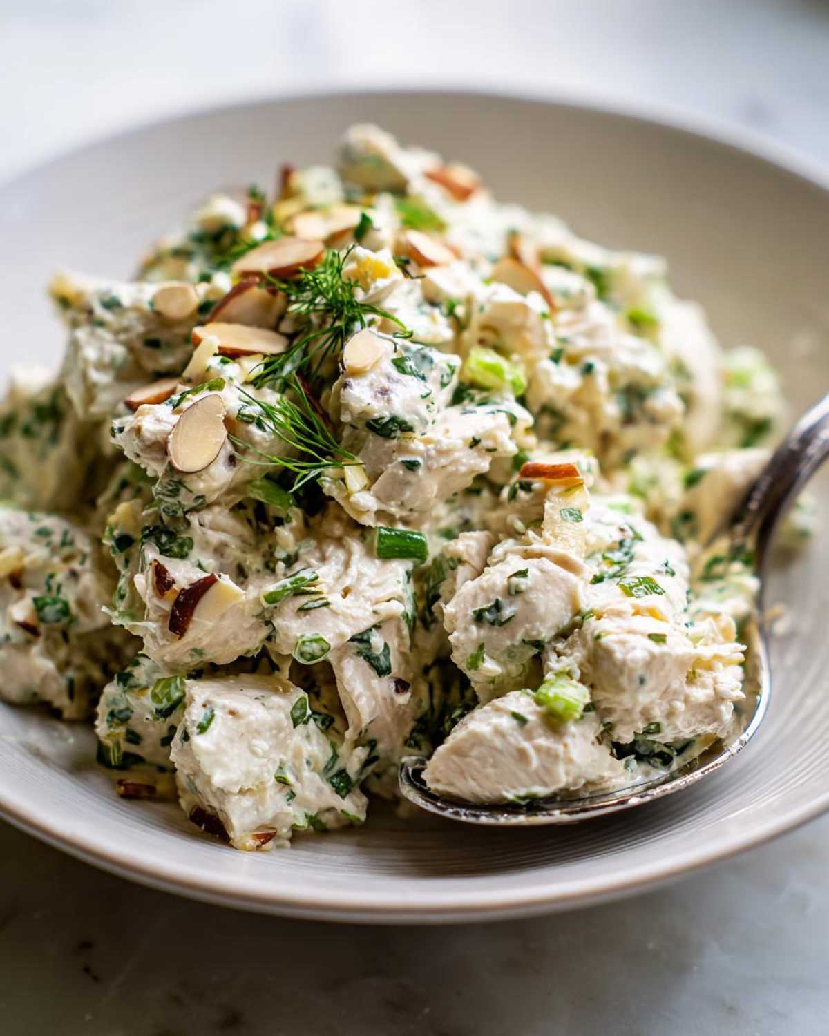 A close-up of creamy Keto Lemon Herb Chicken Salad mixed with green herbs and topped with sliced almonds, served in a light bowl.