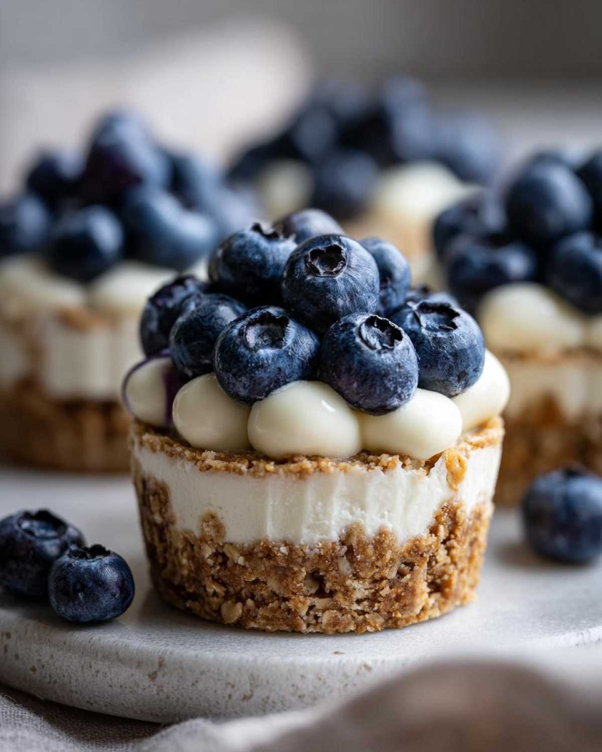 A single, perfectly formed No-Bake Blueberry Cheesecake Oat Cup topped with fresh blueberries and cream dollops.