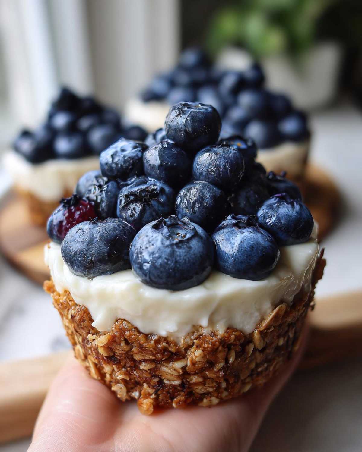 A hand holding one of the No-Bake Blueberry Cheesecake Oat Cups, topped generously with fresh blueberries.