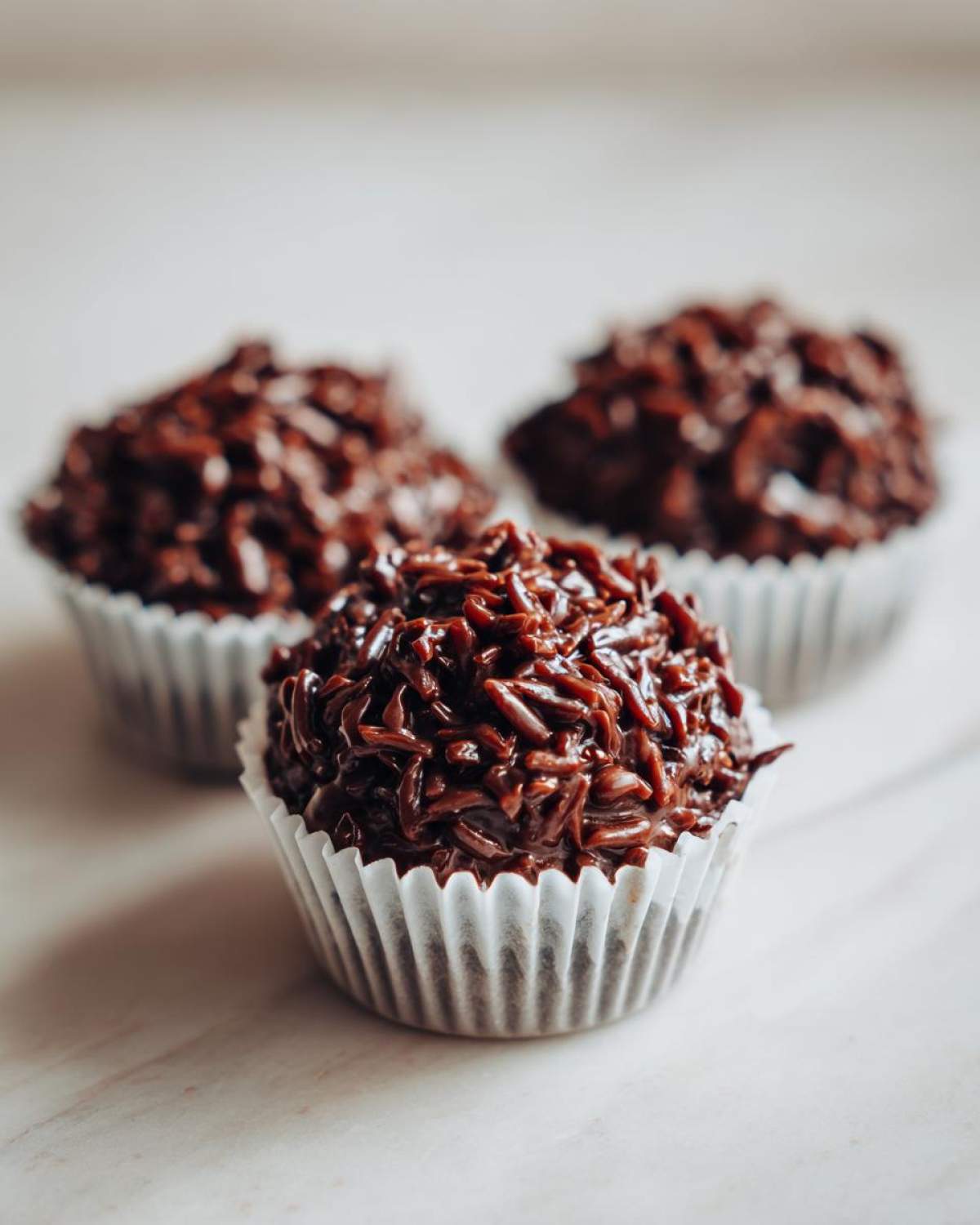 Three No-Bake Chocolate Coconut Protein Cups coated in chocolate sprinkles, resting in white paper liners.