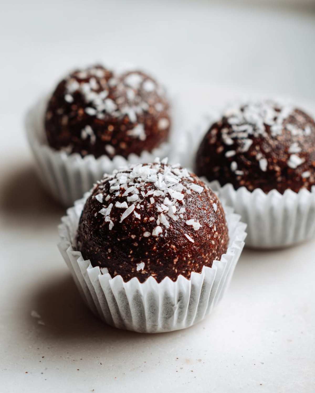 Three dark chocolate protein balls topped with shredded coconut, presented in white paper liners.