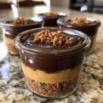 A close-up of one of the No-Bake Chocolate Peanut Butter Pie Jars, showing layers of crust, peanut butter filling, and chocolate topping.