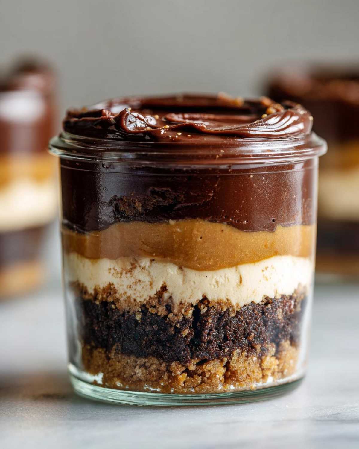 A close-up of one of the No-Bake Chocolate Peanut Butter Pie Jars showing distinct layers of crust, cake, peanut butter filling, and chocolate topping.