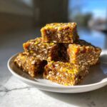 A stack of six chewy No-Bake Lemon Almond Date Bars garnished with bright yellow lemon zest.