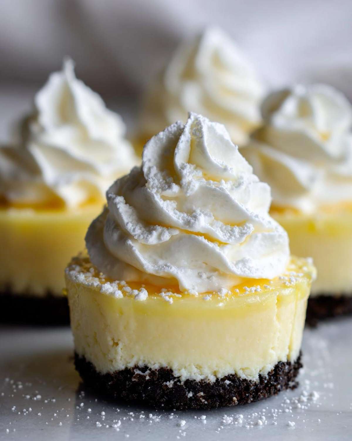 A close-up of a single No-Bake Lemon Cream Pie Cup topped with a swirl of whipped cream and powdered sugar.