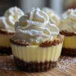 A close-up of a No-Bake Lemon Cream Pie Cup featuring a graham cracker crust, creamy lemon filling, and a swirl of whipped cream dusted with powdered sugar.