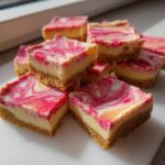 Close-up of stacked squares of No-Bake Lemon Strawberry Cheesecake Bark with a graham cracker crust and pink swirl topping.