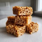 A stack of five gooey, golden No-Bake Peanut Butter Rice Cereal Bars resting on a light countertop.