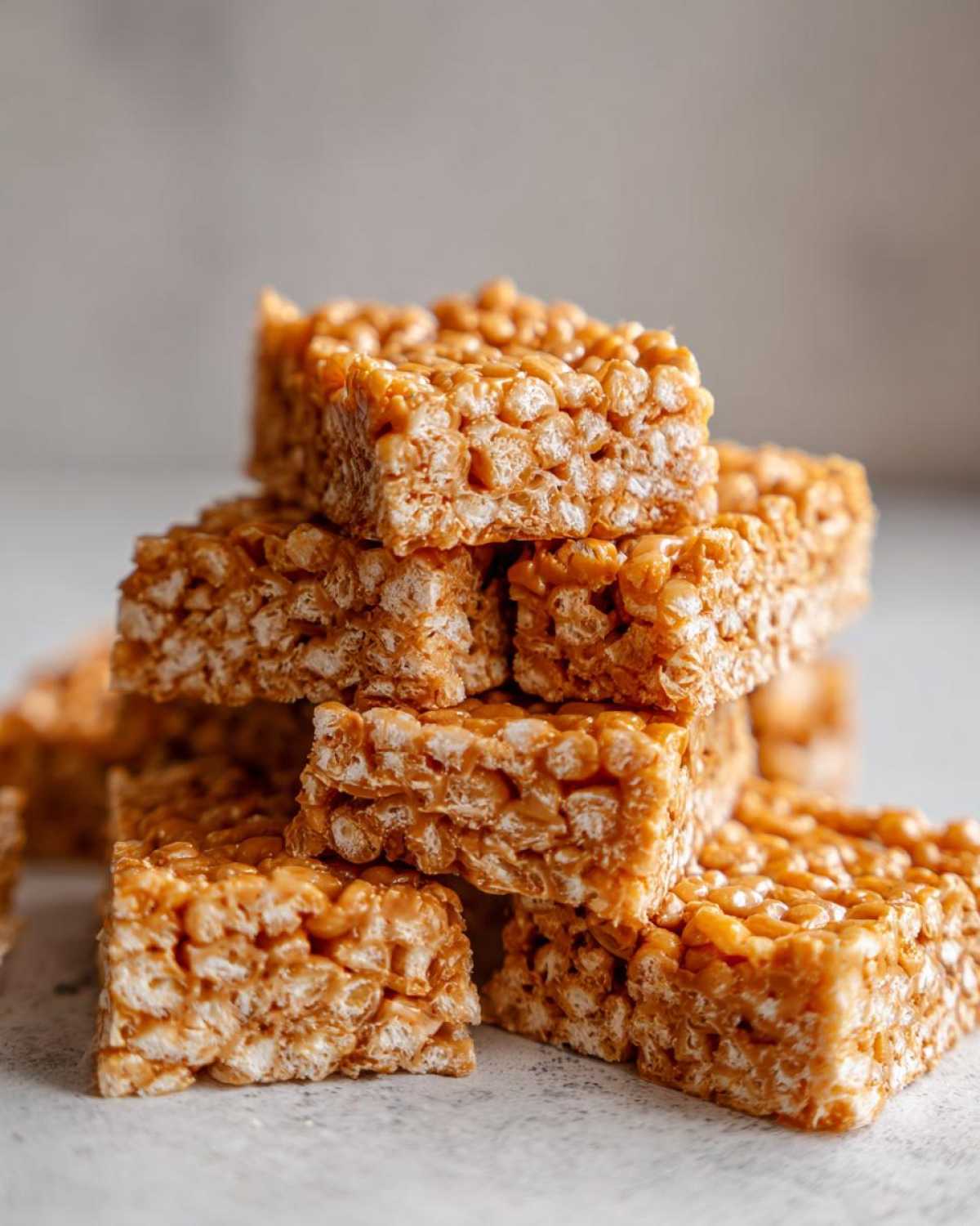 A close-up stack of golden brown No-Bake Peanut Butter Rice Cereal Bars, showing the texture of the puffed rice.