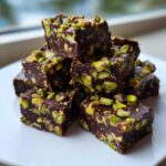 A stack of rich, dark No-Bake Pistachio Chocolate Fudge Squares generously studded with bright green pistachios.