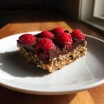 A single serving of No-Bake Raspberry Chocolate Oat Slice topped with fresh raspberries, sitting on a white plate.