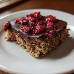 A square serving of No-Bake Raspberry Chocolate Oat Slice with a thick chocolate topping and dried raspberries.