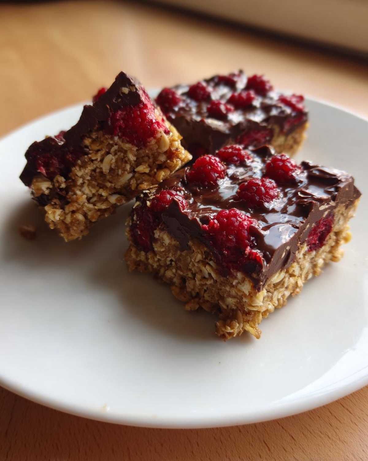 Three squares of No-Bake Raspberry Chocolate Oat Slice featuring a thick oat base, raspberries, and a melted chocolate topping.