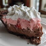 A decadent slice of No-Bake Strawberry Chocolate Pudding Pie showing layers of chocolate, pink strawberry mousse, and whipped cream.