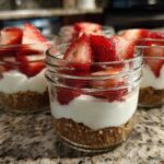 Close-up of several No-Bake Strawberry Cream Pie Jars layered with graham cracker crust, cream filling, and fresh strawberries.