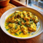 Close-up of bite-sized pieces of One-Pan Creamy Coconut Lime Chicken in a rich, yellow sauce, garnished with fresh cilantro.