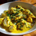 Close-up of chunks of One-Pan Creamy Coconut Lime Chicken coated in a vibrant yellow sauce and topped with fresh cilantro.