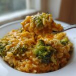 A spoonful of creamy, cheesy One-Pot Creamy Broccoli Cheddar Rice being lifted from a white bowl.
