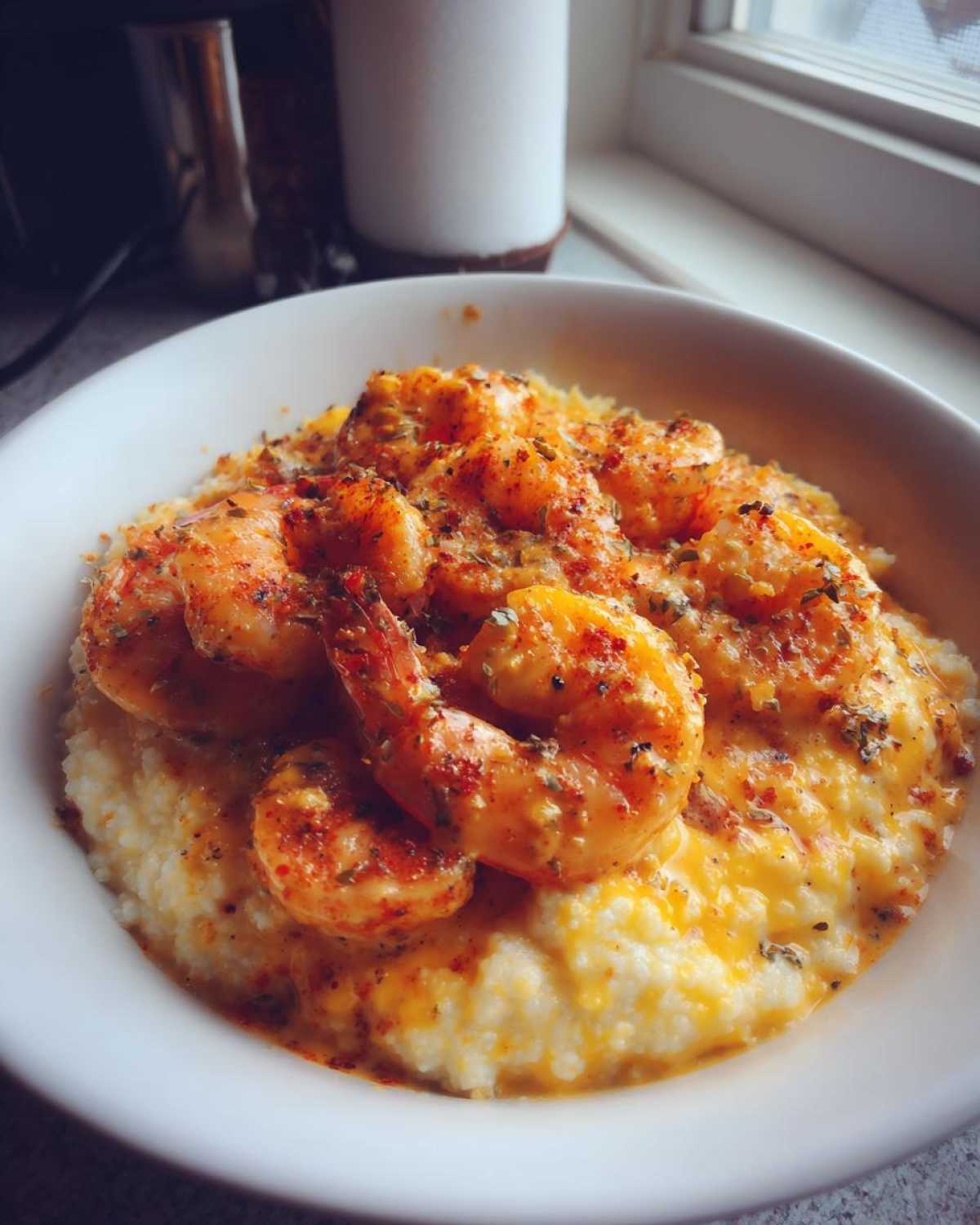 A close-up of a white bowl filled with creamy One-Pot Creamy Cajun Shrimp and Grits, topped with seasoned shrimp.