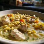 Close-up of a bowl of One-Pot Creamy Lemon Chicken Noodle Soup with chunks of chicken, spiral pasta, and carrots.