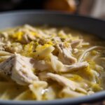 Close-up of tender shredded chicken and egg noodles in a rich broth, topped with lemon zest for One-Pot Creamy Lemon Chicken Noodle Soup.