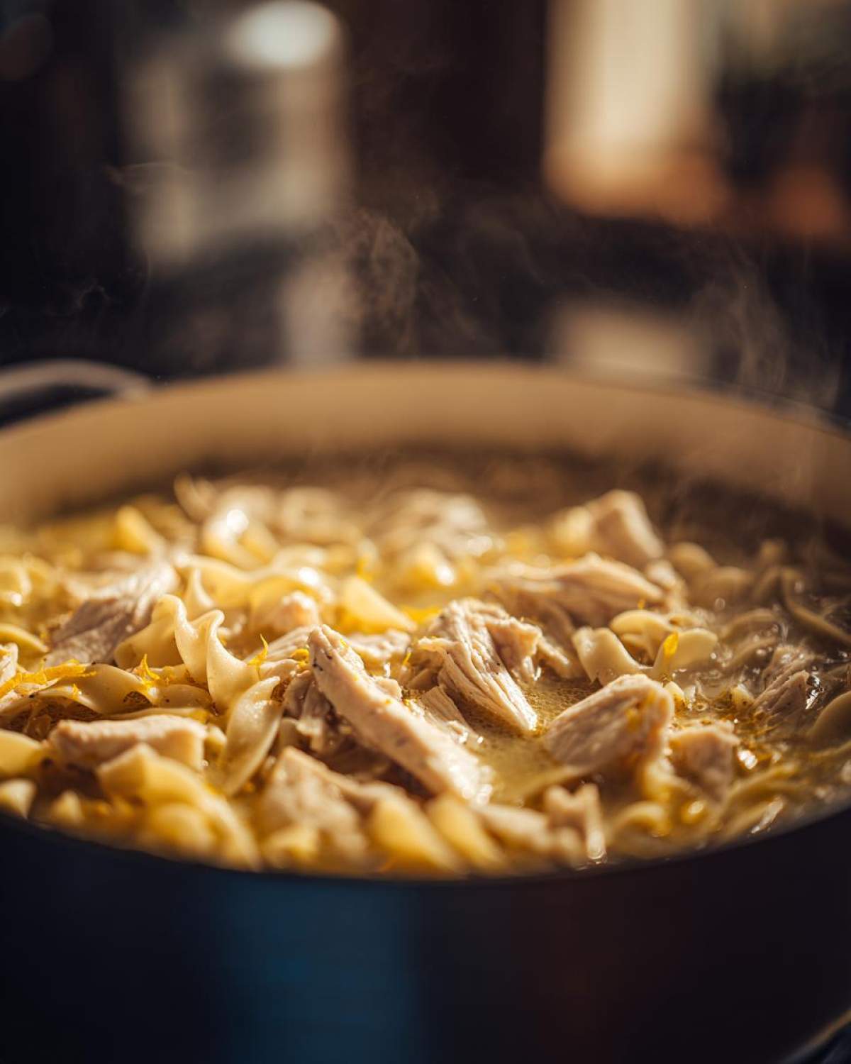 Close-up of steaming One-Pot Creamy Lemon Chicken Noodle Soup with shredded chicken and egg noodles.