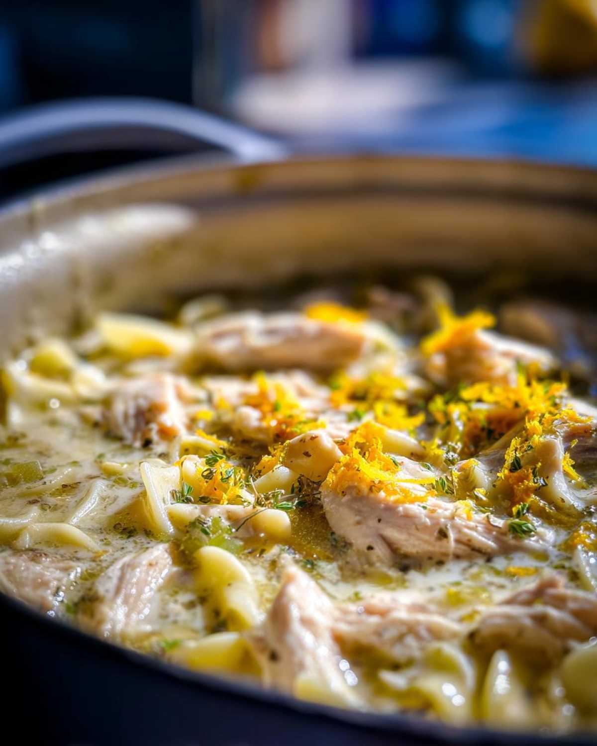 Close-up of One-Pot Creamy Lemon Chicken Noodle Soup garnished with bright lemon zest and thyme.
