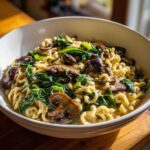 A white bowl filled with One-Pot Creamy Mushroom Spinach Ramen, featuring curly noodles, sautéed mushrooms, and wilted spinach.