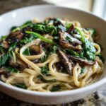 Close-up of One-Pot Creamy Mushroom Spinach Ramen noodles coated in sauce with wilted spinach and sliced mushrooms.