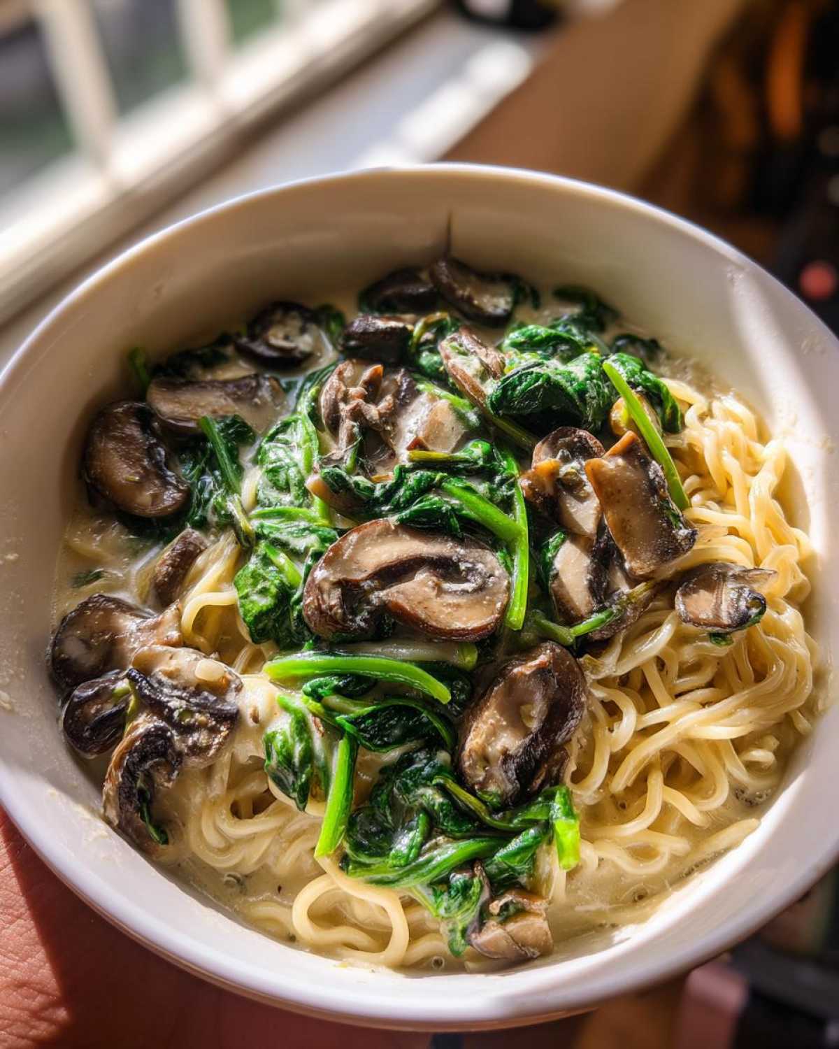 Close-up of One-Pot Creamy Mushroom Spinach Ramen with noodles, dark mushrooms, and bright green spinach in a white bowl.