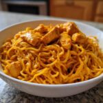 A white bowl filled with One-Pot Creamy Thai Red Curry Noodles topped with chunks of chicken.