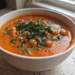 Close-up of a white bowl filled with One-Pot Creamy Tomato Basil Chickpea Stew, topped with fresh basil.