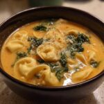A close-up of a dark bowl filled with One-Pot Creamy Tortellini Minestrone, featuring cheese tortellini, spinach, and grated Parmesan.