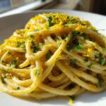 A close-up of a serving of One-Pot Creamy White Bean Lemon Pasta, topped with fresh parsley and bright yellow lemon zest.