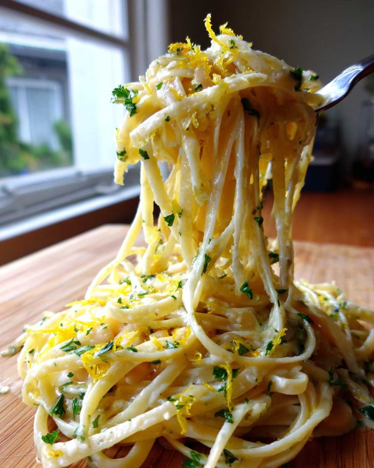Close-up of One-Pot Creamy White Bean Lemon Pasta being lifted high on a fork, topped with lemon zest and parsley.